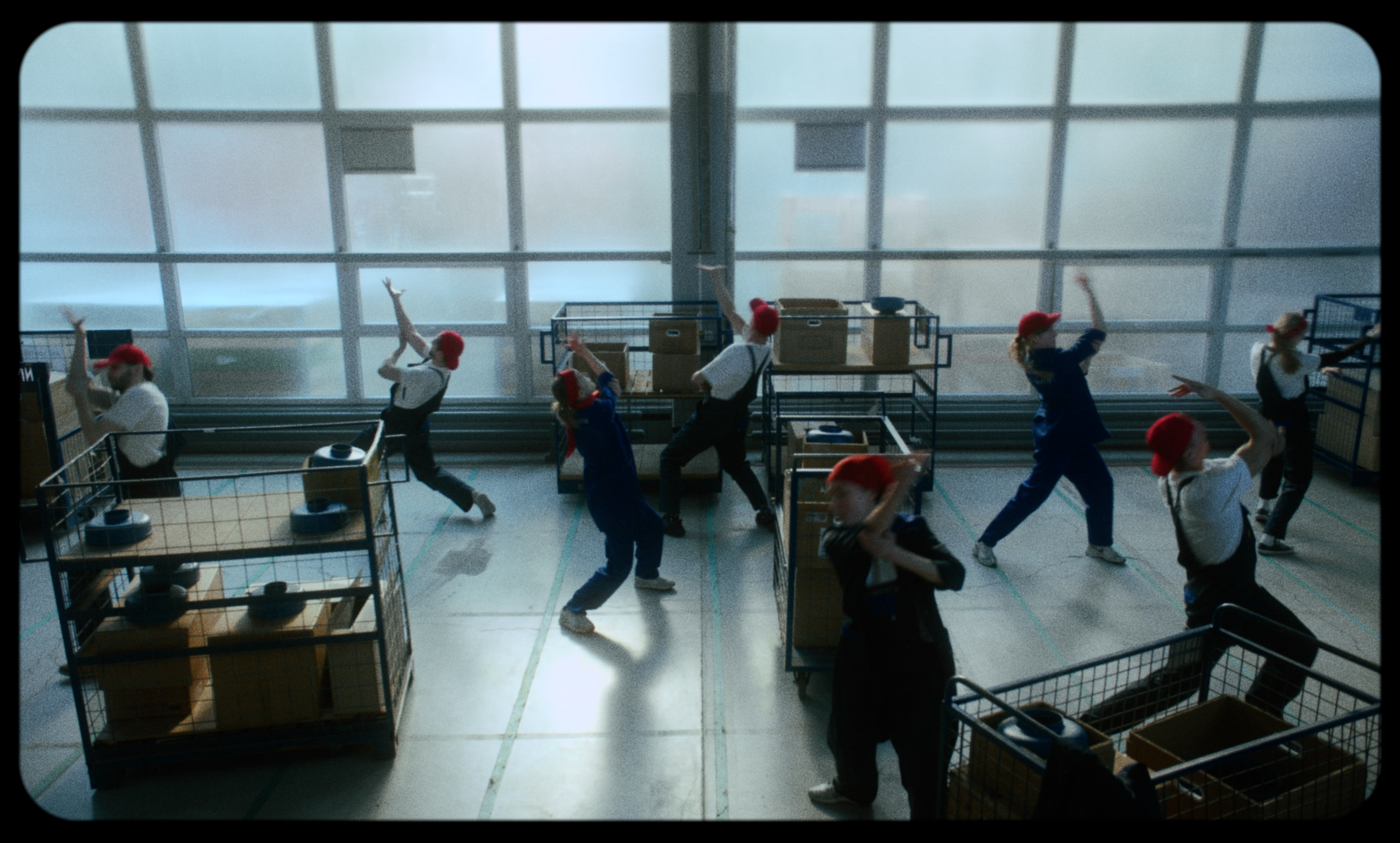 Workers in red caps move in synchronized gestures on a factory floor — a still from Kira’s Dream.