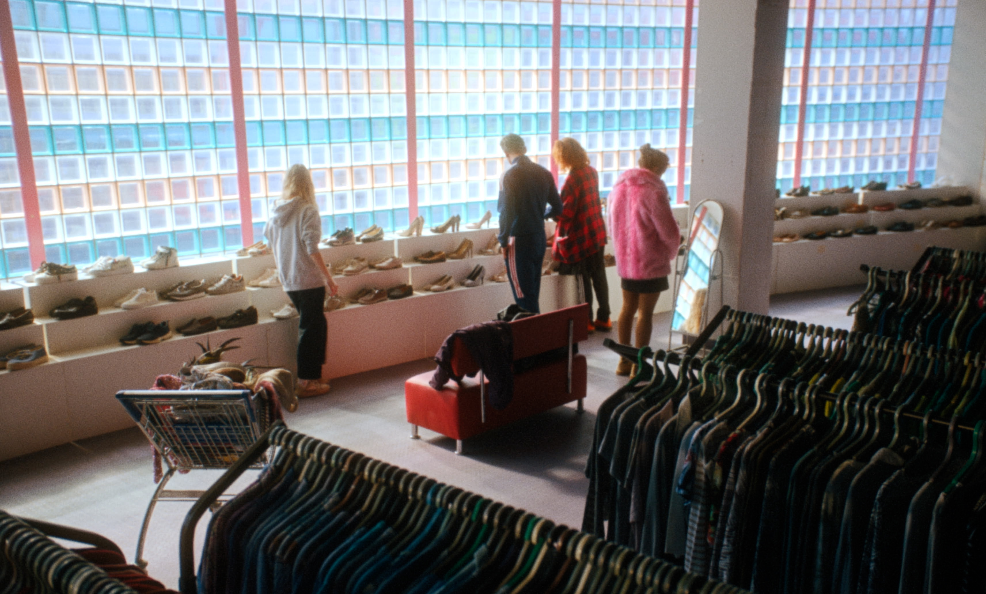Young women browse shoes in a bright secondhand store with clothing racks — a still from Kira’s Drea