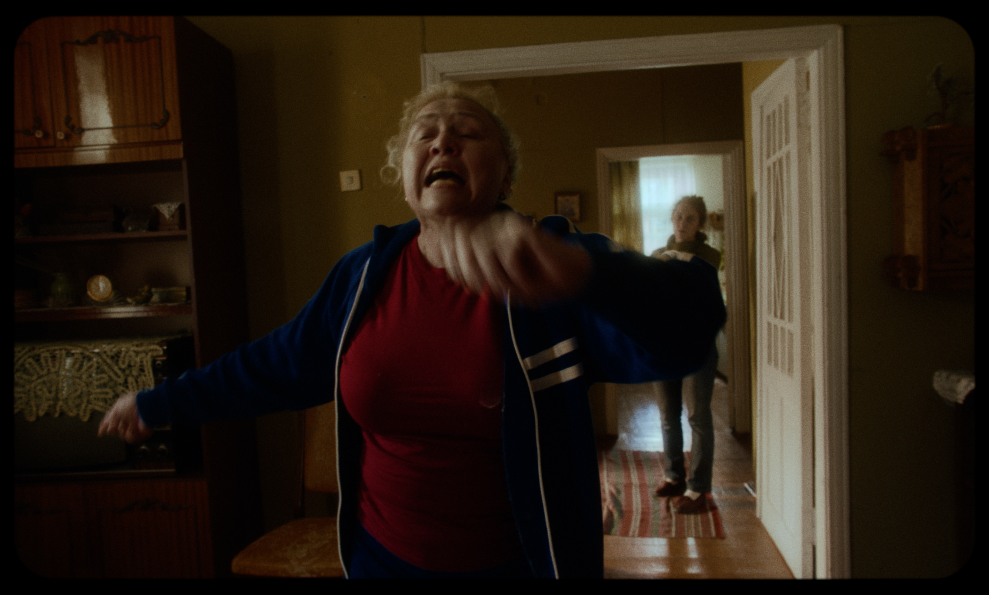 A woman shouts in a small apartment while another person stands in the doorway — a still from Kira’s