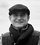 Smiling man in a flat cap and jacket, black and white photo.